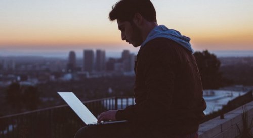 Ein Mann sitzt mit seinem Laptop auf einem Dach.