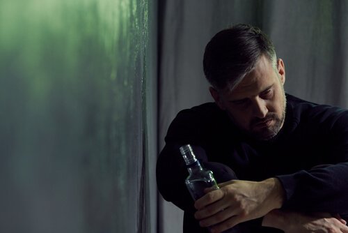 Ein verzweifelter Mann hält eine Flasche Alkohol in der Hand.