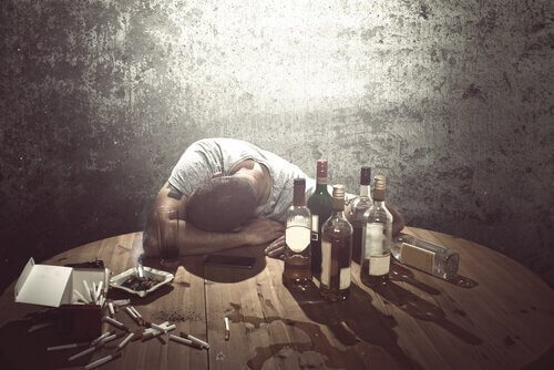 Mann schläft am Tisch mit Flaschen und Zigaretten.