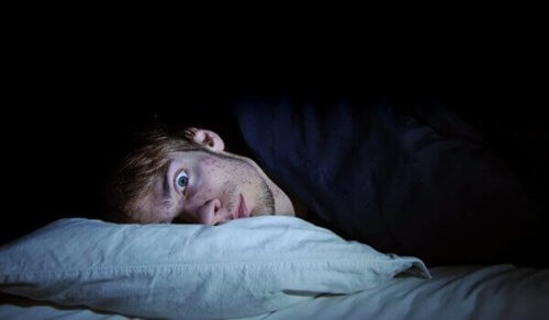 Ein Mann liegt mit weit geöffneten Augen im Bett. 