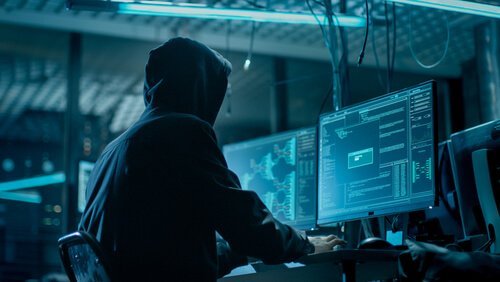 Ein Mann sitzt vor einem Computerbildschirm in einem dunklen Raum. 