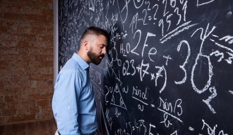 Erschöpfter Lehrer lehnt seinen Kopf an die vollgeschriebene Tafel.