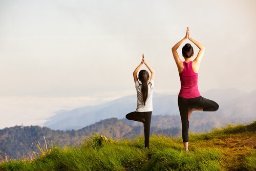 Eine Mutter und ihr Kind stehen auf einem Berg, während sie eine Yoga-Übung machen. 
