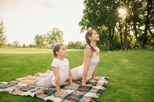 Eine Mutter und ihr Kind sind im Park und machen Yoga auf einer Decke.