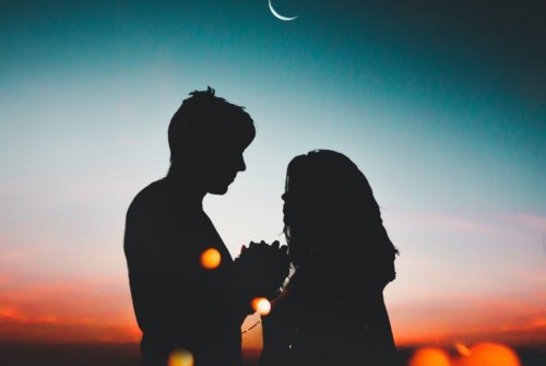 Ein Paar steht zusammen vor einem Sonnenuntergang, während der Mond aufgeht. 