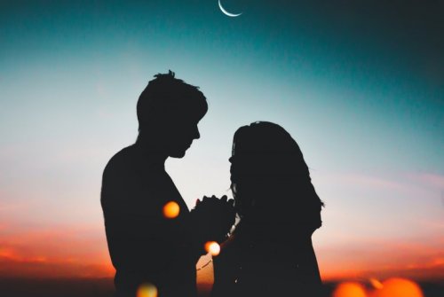 Ein Paar steht zusammen vor einem Sonnenuntergang, während der Mond aufgeht.