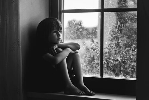 Kind, das traurig bei einem Fenster sitzt