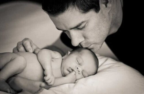 Ein junger Vater küsst sein Baby, das im Bett liegt und schläft.