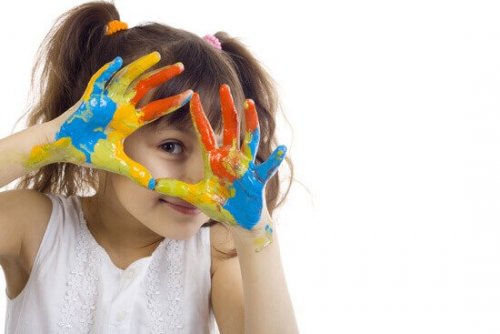 Ein Mädchen hält seine Hände voller Fingerfarbe glücklich in die Kamera. 