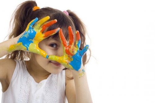 Ein Mädchen hält seine Hände voller Fingerfarbe glücklich in die Kamera.