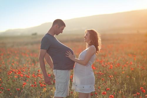 Ein schwangerer Mann und seine schwangere Frau stehen in einem Mohnblumenfeld.