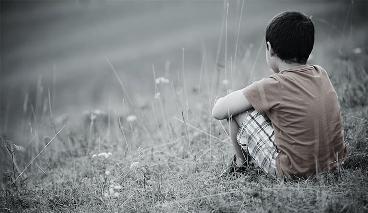 Trauriger Junge sitzt allein auf einer Wiese.