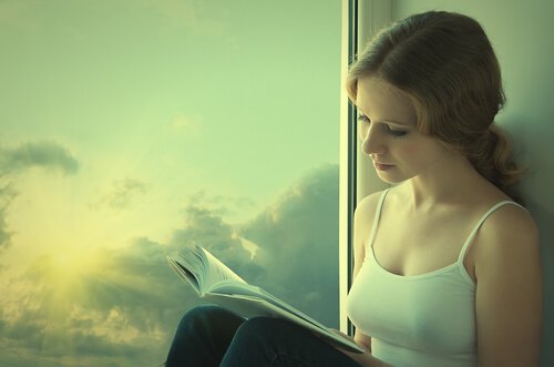 Eine Frau sitzt am Fenster und liest ein Buch.