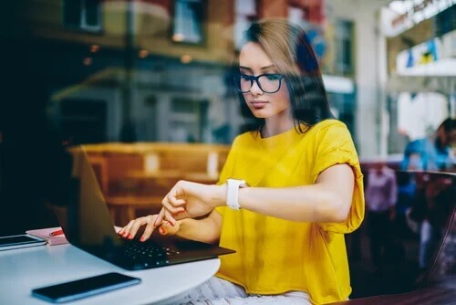 Frau arbeitet am Rechner und schaut auf die Uhr