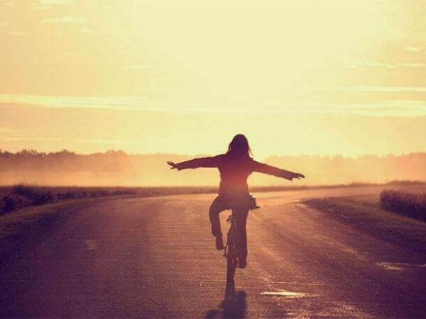 Aufgeschobenes-Glück-Syndrom: Machen wir, was uns glücklich macht: Eine Frau fährt Fahrrad im Sonnenuntergang.