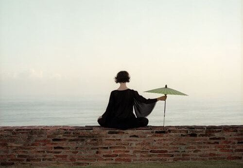 Eine Frau sitzt mit einem Regenschirm am Meer.