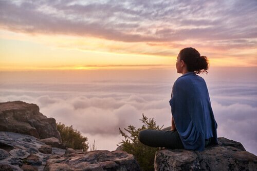 Eine Frau sitzt auf einem Berg über den Wolken.