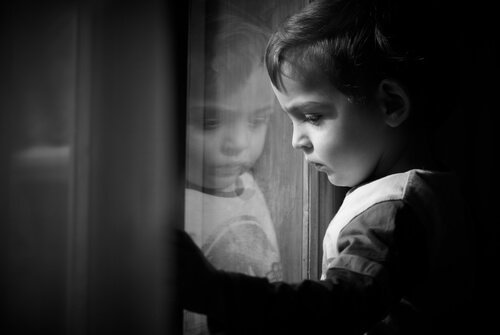 Ein kleiner Junge schaut traurig aus dem Fenster. 