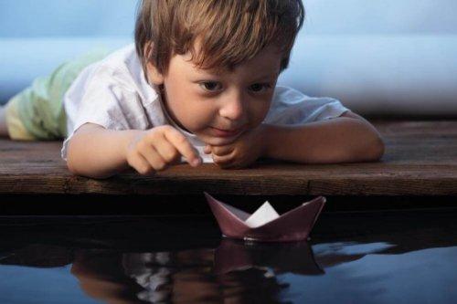 Kleiner Junge spielt mit einem gefalteten Papierschiff.