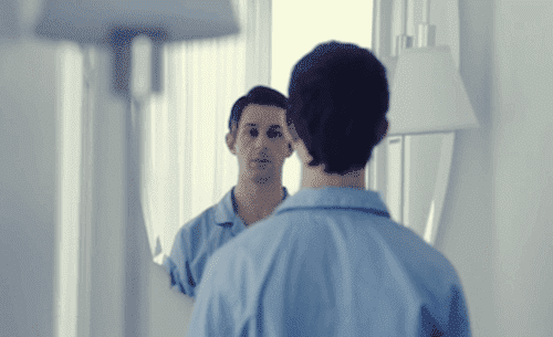 Ein Mann betrachtet sich im Spiegel. 