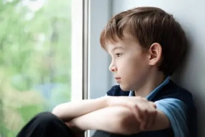 Junge schaut traurig aus dem Fenster