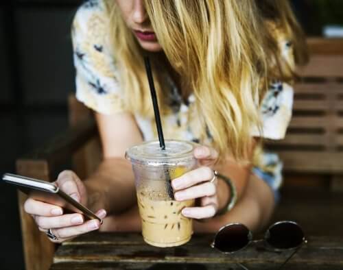 Frau mit Telefon trinkt Eiskaffee