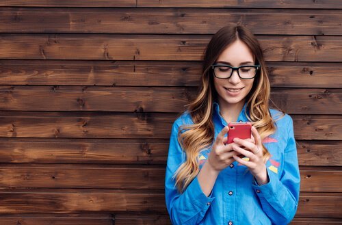 Junge Frau vor einer Wand schaut auf ihr Telefon