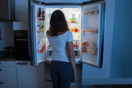 Frau, die nachts vor dem Kühlschrank steht