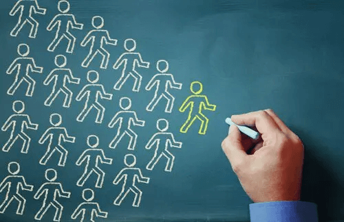 Viele weiße Kreidemännchen laufen einem gelben hinterher