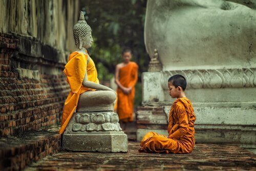 Junger Mönch sitzt vor einer Statue von Buddha