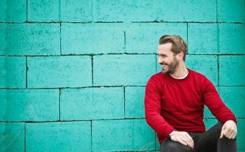 Ein Mann mit einem roten Pulli lehnt an einer Wand. 
