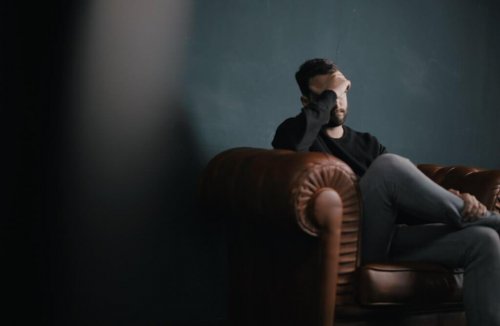 Mann sitzt auf einer Couch und stützt seinen Kopf auf seine Hand