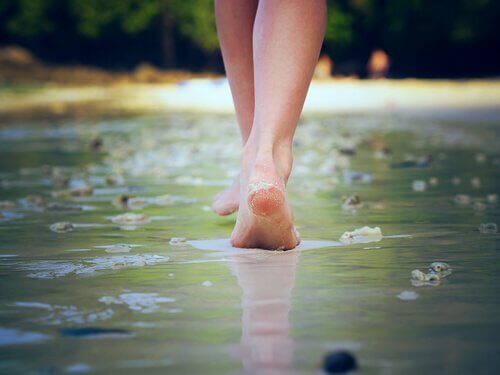 Ein Foto, das ein Paar Füße zeigt, die entlang eine Straße gehen, die in einer dünnen Schicht Wasser bedeckt wird.