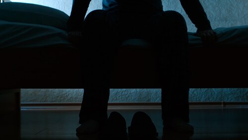 Mann, der auf dem Bett leidet unter unruhigem Beinsyndrom sitzt.