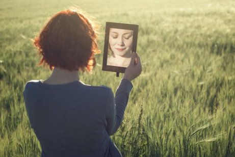 Eine Frau, die auf einem Feld steht und sich selbst im Spiegel betrachtet, während sie darüber nachdenkt, den Weg zur Selbsterkenntnis einzuschlagen.