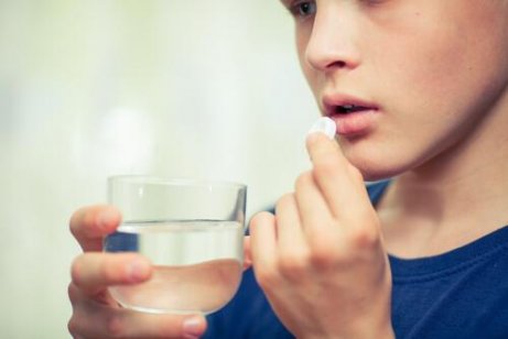 Ein junger Mensch, der ein Glas Wasser hält, während er sich darauf vorbereitet, eine Pille einzunehmen, symbolisiert den Gebrauch von Psychopharmaka bei Kindern und Jugendlichen.