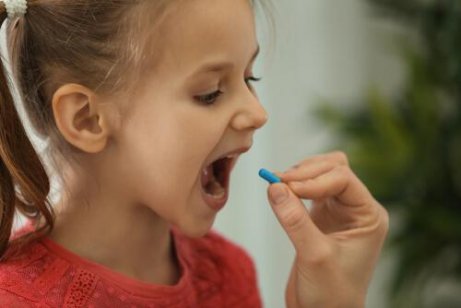 Ein Kind öffnet den Mund weit, um eine Pille einzunehmen.
