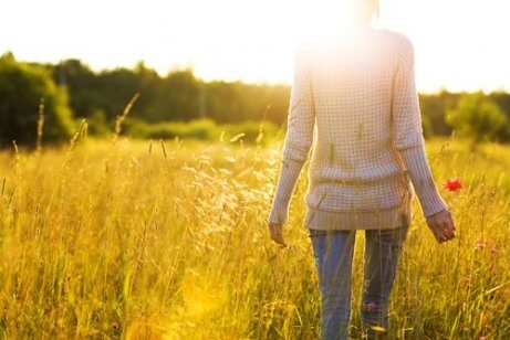 Eine Person, die vom Nacken aus gesehen durch ein sonniges Feld läuft und glücklich ist, ohne Angst zu leben.