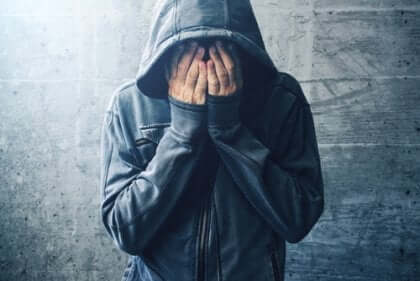 Ein Mann, der einen Hoodie mit den Händen über Gesicht trägt.