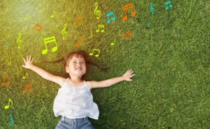 Ein kleines Mädchen, das auf dem Gras hört Musik liegt.