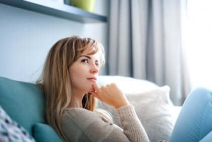Eine Frau sitzt auf der Couch und denkt nach.