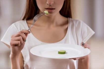 Essstörungen - Mädchen mit Magersucht isst ein Stück Gurke