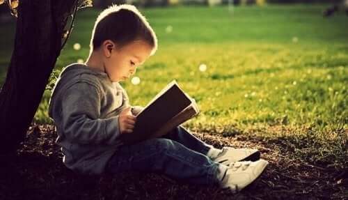 Ein kleiner Junge sitzt unter einem Baum und liest