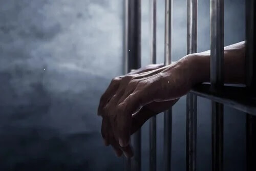 Hände einer Person hinter Gittern. Keine Kaution