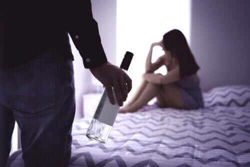 Co-Abhängigkeit - Mann mit Flasche vor einer Frau auf dem Bett
