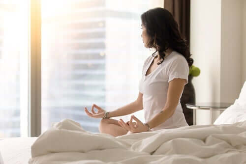 Mit Meditation besser einschlafen - Frau meditiert auf dem Bett