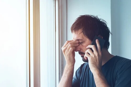 Ein Mann am Handy reibt sich gestresst die Augen.