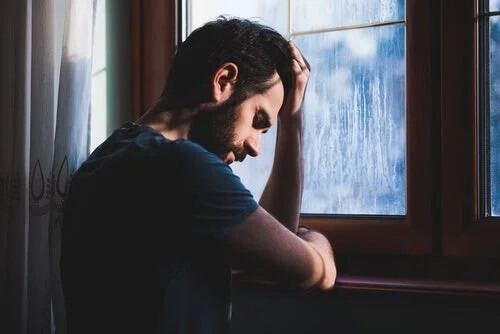 Ein trauriger Mann vor einem Fenster an einem regnerischen Tag.