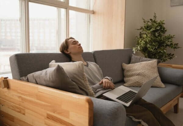 Extreme Müdigkeit - Mann schläft auf Sofa mit Laptop auf den Beinen